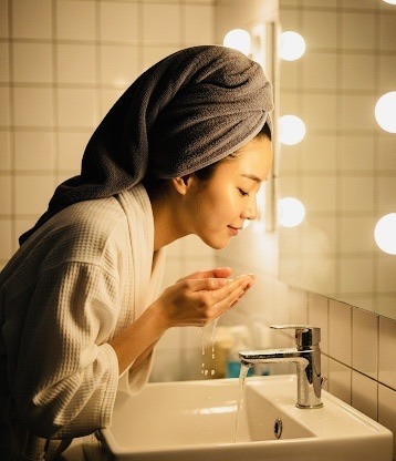 Femme coréenne se rinçant le visage dans une salle de bain, rituel apaisant d’une routine beauté coréenne