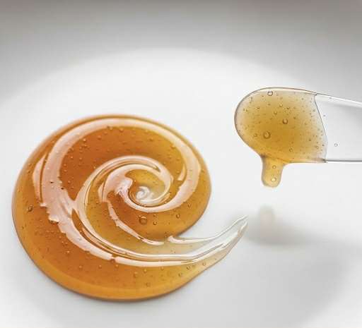 Texture d’une ampoule coréenne au propolis, dorée et visqueuse, déposée en spirale sur une assiette blanche